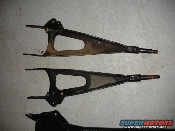 Two suspension control arms laid out on a concrete floor