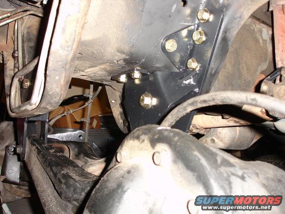 Black lift bracket bolted to vehicle frame with gold bolts. Suspension components visible