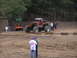 1995 Ford Bronco - A custom orange off-road jeep with oversized tires is parked in a dirt lot, with a tractor and spectators in the background.