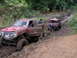 1995 Ford Bronco - Two off-road vehicles are stuck in deep mud on a trail surrounded by trees.
