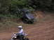 1995 Ford Bronco - An ATV rider passes a dark SUV that is stuck on a muddy hill in an off-road park.