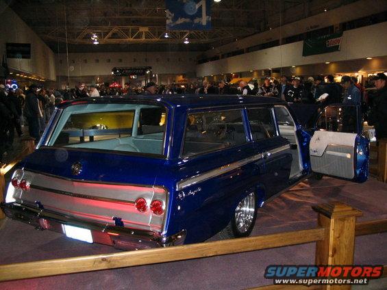 Blue station wagon with chrome trim and custom wheels, doors open, inside a building with people around