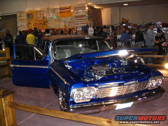 Blue sedan with hood open, chrome grille, and dual headlights. Interior visible