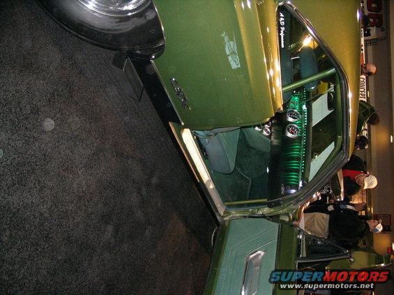 Interior of a green muscle car with roll cage, gauges, and custom seats. Text on door reads '4.6 Performance'