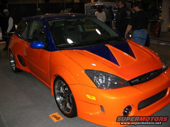 Orange and blue hatchback with custom body kit and aftermarket wheels, viewed from the front three-quarter angle