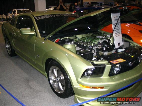 Green 2005 Ford Mustang with hood open, showing engine and a display sign