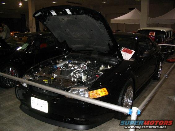 Black coupe with hood open, chrome wheels, and exposed engine. A sign is visible on the dashboard