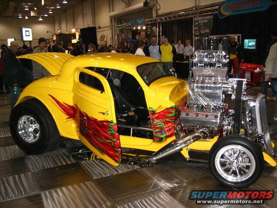 Yellow custom hot rod with flames on doors and a large chrome engine exposed