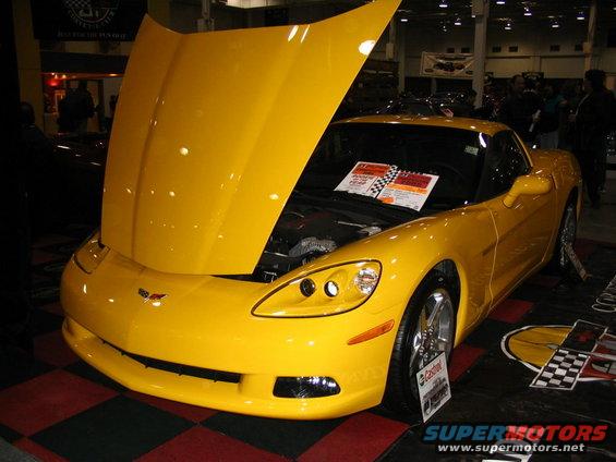 Yellow Chevrolet Corvette with hood open, showing engine. Displayed indoors on a checkered mat
