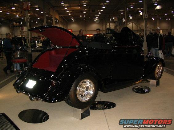 Black convertible hot rod with red interior, hood open, on display