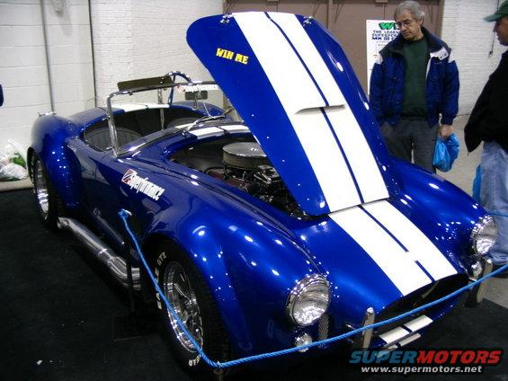Blue convertible with white racing stripes, hood open, showing engine. Text 'WIN ME' on hood