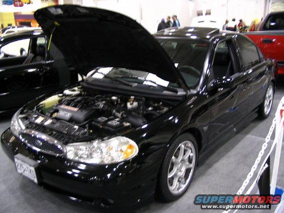 Black sedan with hood open, showing engine. Another black car is to the left, red truck to the right