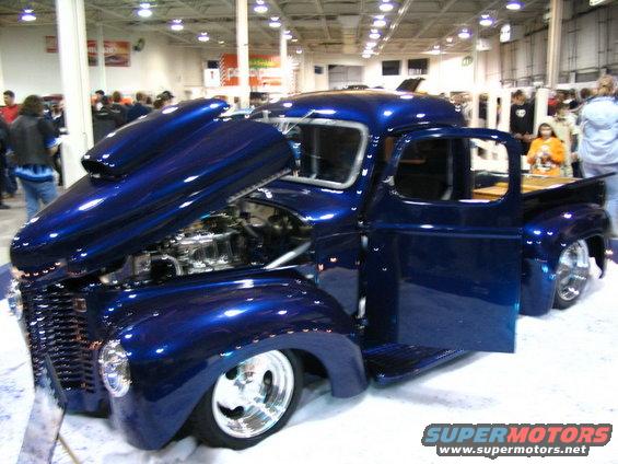 Blue hot rod pickup truck with hood open, showing engine. Door is open