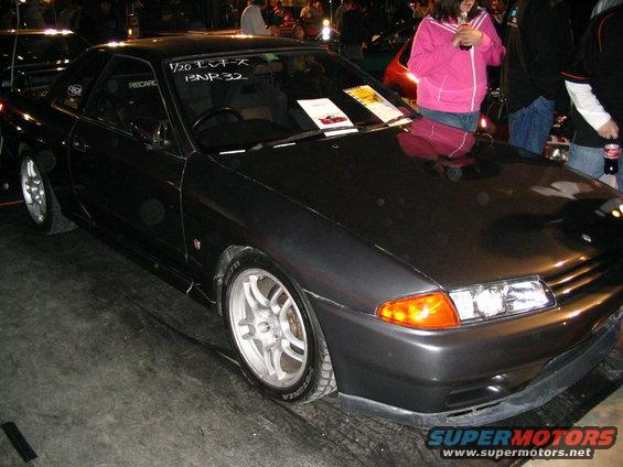 Dark grey coupe with aftermarket wheels and racing seats visible through the window. Text on windshield reads '1/20 EV-X BNR32'