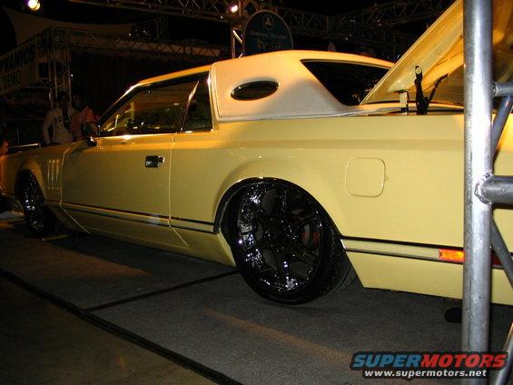 Yellow coupe with vinyl top and large chrome wheels, trunk open