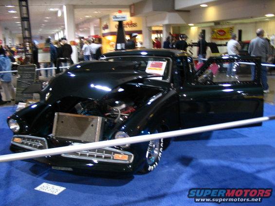 Dark green custom pickup truck with hood open, showing engine and radiator. Door is ajar