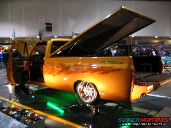 Orange pickup truck with custom flames and open tonneau cover, green underglow, and chrome wheels