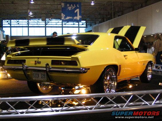 Yellow 1969 Camaro Z/28 with black stripes, custom wheels, and a spoiler. License plate reads SICK 228