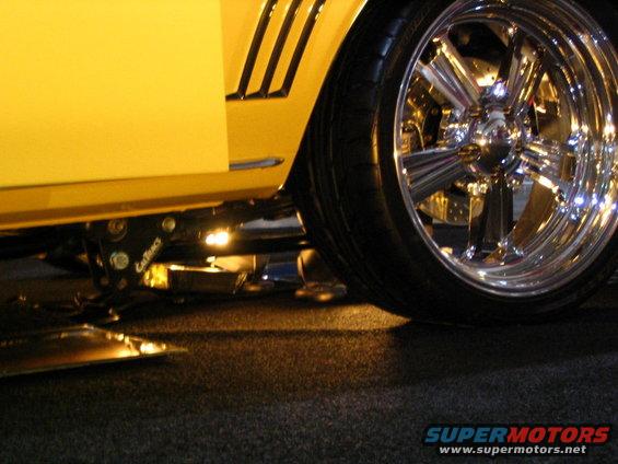 Yellow car side view showing custom suspension and large chrome wheel