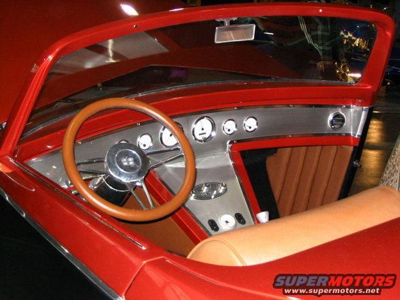 Red custom hot rod interior with wood steering wheel, chrome gauges, and tan seats