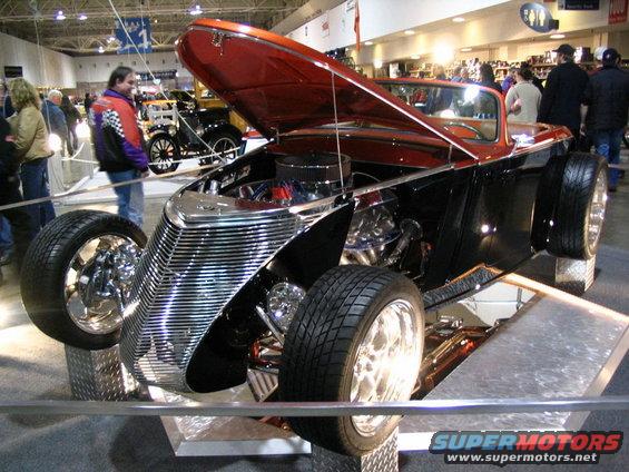 Custom hot rod with chrome grille, orange hood open revealing engine, and exposed front wheels