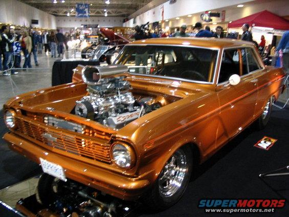 Orange hot rod with a large supercharger and exposed engine, viewed from the front three-quarter angle