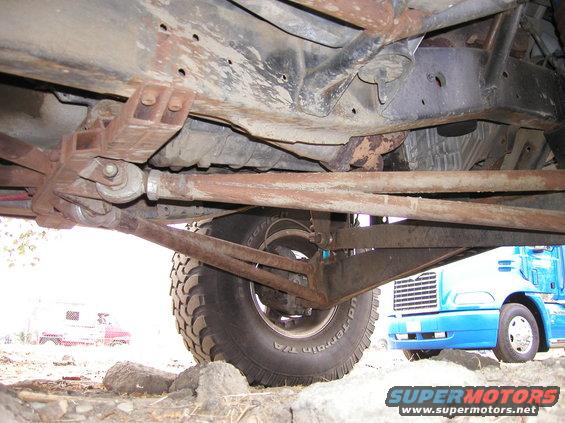Undercarriage of a rusty vehicle with a blue semi-truck in the background