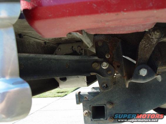 Red vehicle body above black trailer hitch receiver and frame. Visible rust on metal components