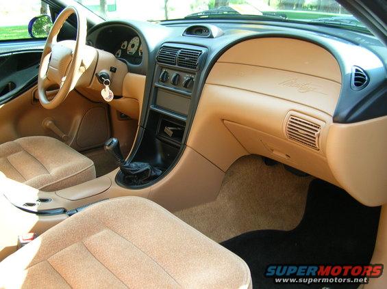 Interior of a 1995 Ford Mustang, showing tan seats, dashboard, and center console with a manual shifter