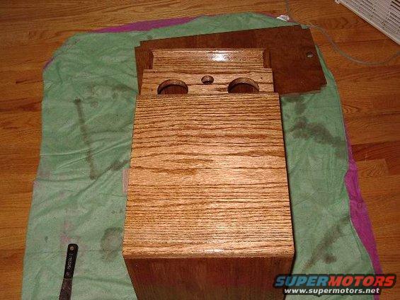 Wooden center console part with two circular cutouts and a smaller central hole, resting on a green cloth on a wooden floor