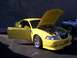 2002 Ford Mustang - A yellow 2002 Ford Mustang is displayed with its hood and driver's door open, parked next to another Mustang.