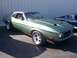2002 Ford Mustang - This green 1971 Ford Mustang coupe features distinctive hood scoops and chrome wheels, parked next to another vehicle.