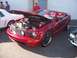 2002 Ford Mustang - A red convertible Mustang is displayed with its hood open, revealing the engine bay. Another vehicle is parked nearby.