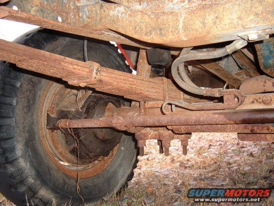Close-up of heavily rusted leaf spring, axle, and tire from an old vehicle