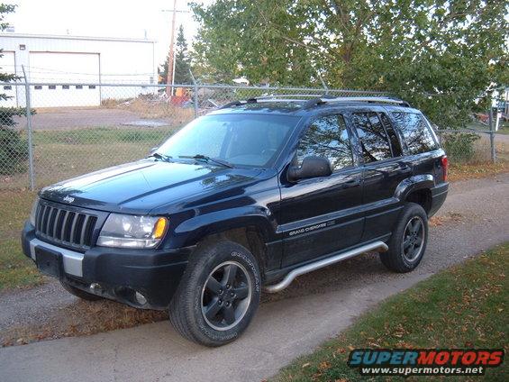 Dark blue Jeep Grand Cherokee parked on a dirt path. Has a roof rack and side steps