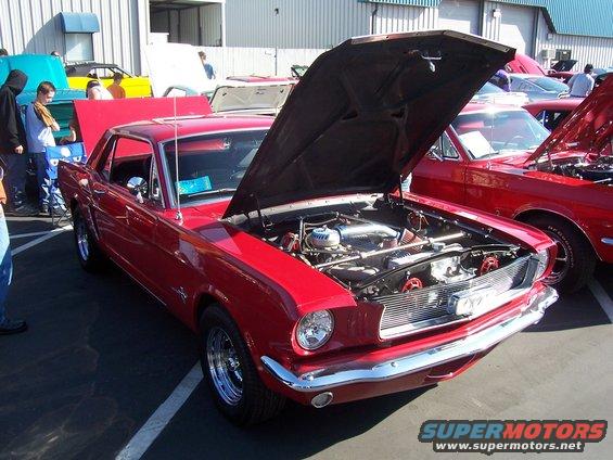 Red 1965 Ford Mustang coupe with hood open, chrome wheels, and custom engine details