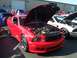 2002 Ford Mustang - A red 2005 Ford Mustang is displayed with its hood open, revealing the engine bay, alongside other vehicles at an outdoor event.