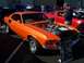 2002 Ford Mustang - This orange 1969 Mustang fastback features chrome wheels and an open hood revealing its engine, displayed at a car show.