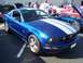 2002 Ford Mustang - A blue Mustang with white racing stripes is parked at an outdoor event, with other vehicles visible in the background.