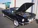 2002 Ford Mustang - A black 1965 Ford Mustang convertible is parked outside a garage with its hood open, revealing the engine bay.
