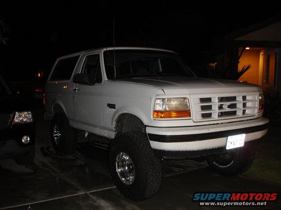 White 1996 Ford Bronco with aftermarket wheels and lifted suspension parked at night