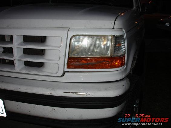 White Ford truck front end, close-up on grille and headlight. Scratched bumper