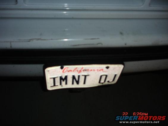 White vehicle rear bumper with California license plate IMNT OJ. Scratches visible on bumper