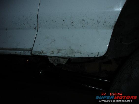 Close-up of the lower body panel and frame of a vehicle. Some rust and dirt are visible