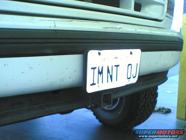 White SUV rear bumper with a license plate reading IMNT OJ and a trailer hitch