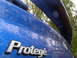 2003 Mazda Protege - Rear view of a blue 2003 Mazda Protege with water droplets on the trunk and a spoiler.