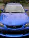 2003 Mazda Protege - Front view of a blue 2003 Mazda Protege parked outdoors on a rainy day.