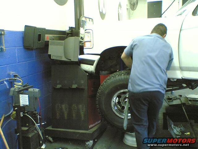 1996 Ford Bronco on a lift with a mechanic working on the front wheel and tire