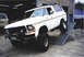 1979 Ford Bronco - Modified white Ford Bronco on a ramp in a garage setting, with another vehicle in the background.