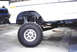 1979 Ford Bronco - The front suspension and wheel of a white SUV are shown, with another vehicle in the background.